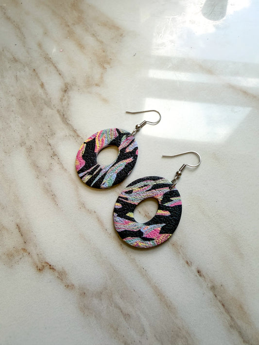 Colorful oval dangles with a center hole cut out. The pattern is black with colorful swirls. They are laying on a marble surface. 
