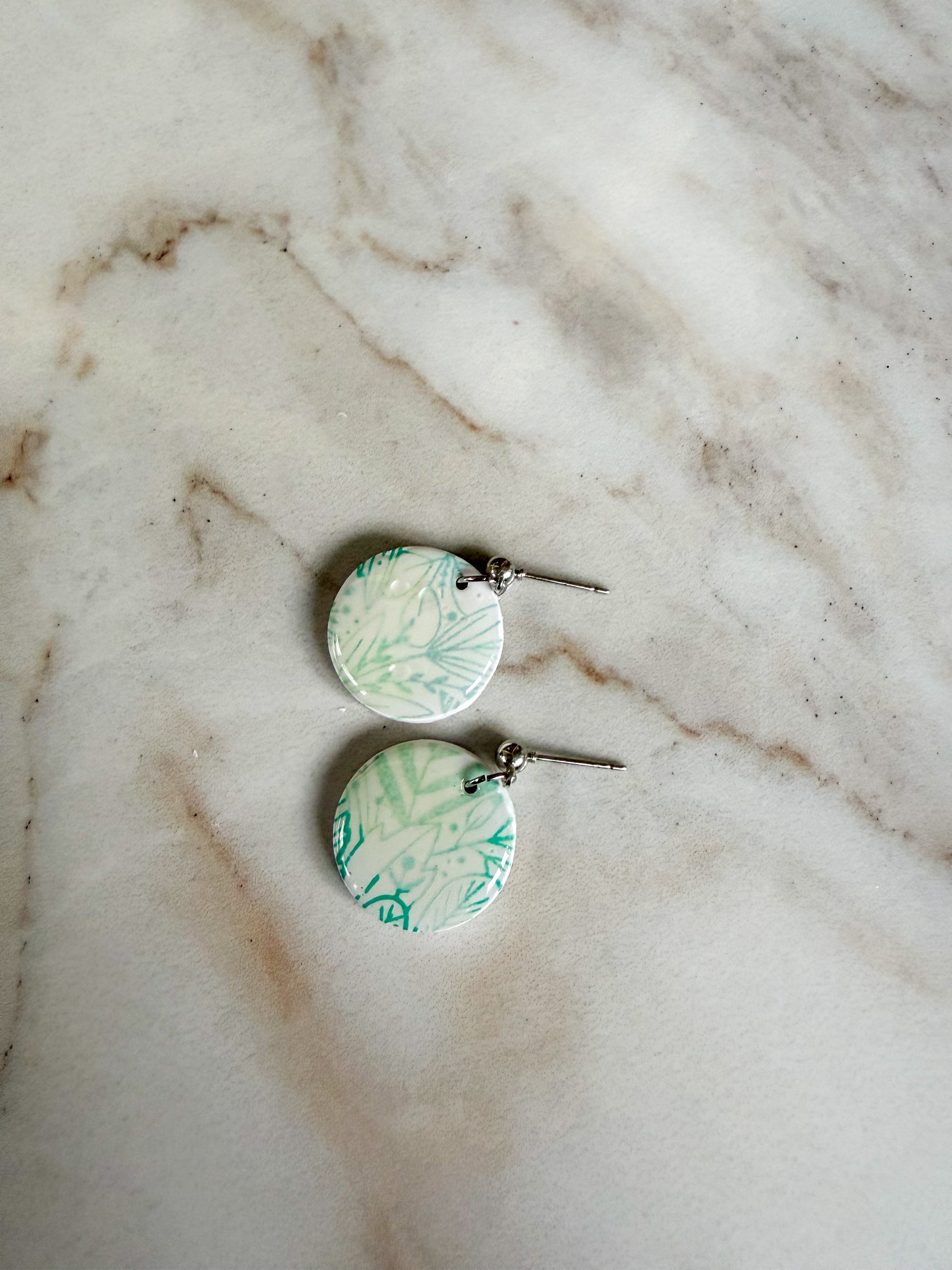 Green and white floral earrings on a marble surface 