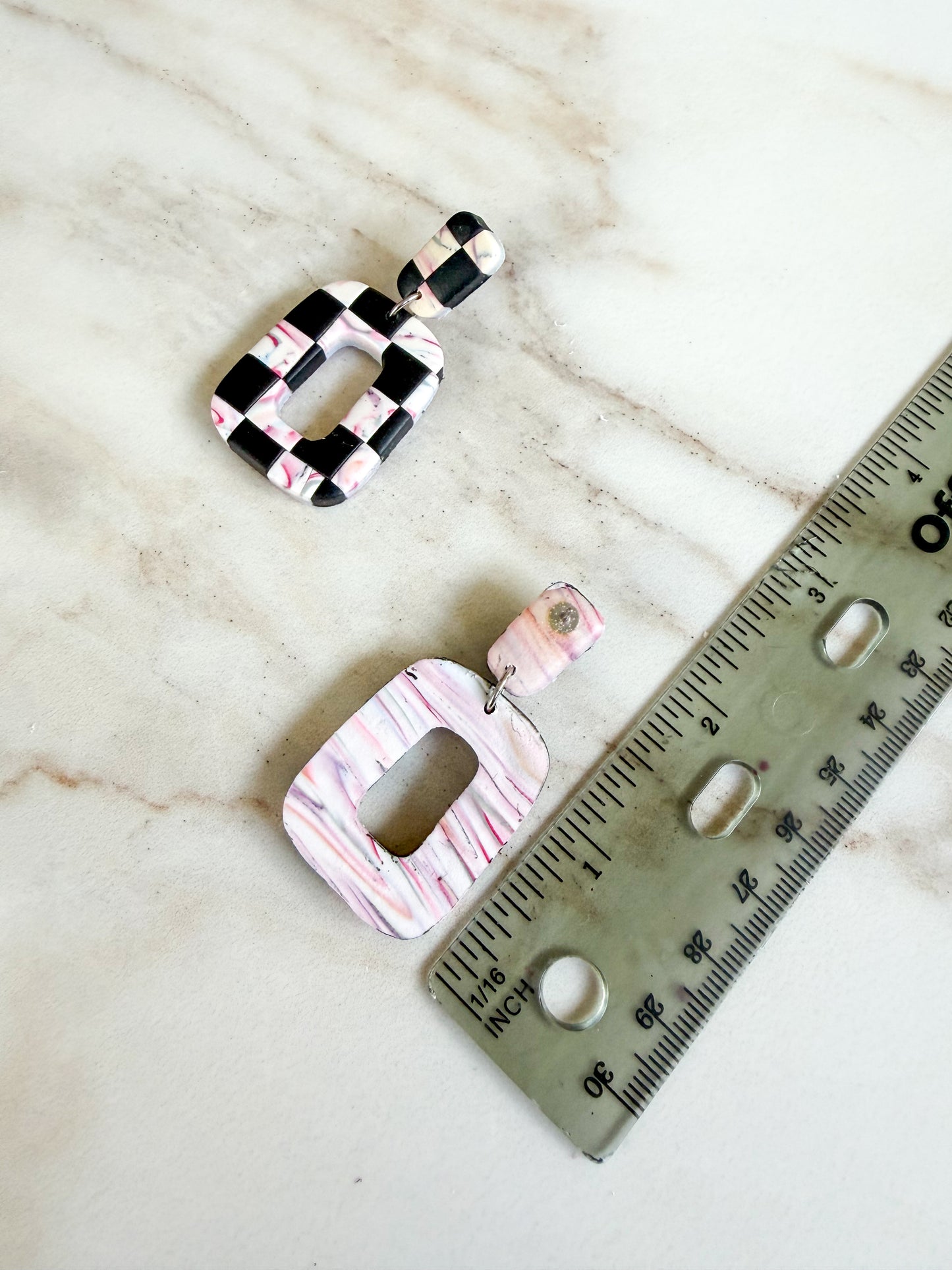 Pair of earrings with a checkered pattern next to a ruler on a marble surface. Approximately 2 inches in length 