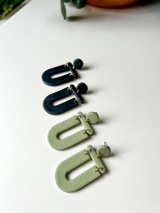 Pair of green and black earrings on a white surface. The pairs are U-shaped