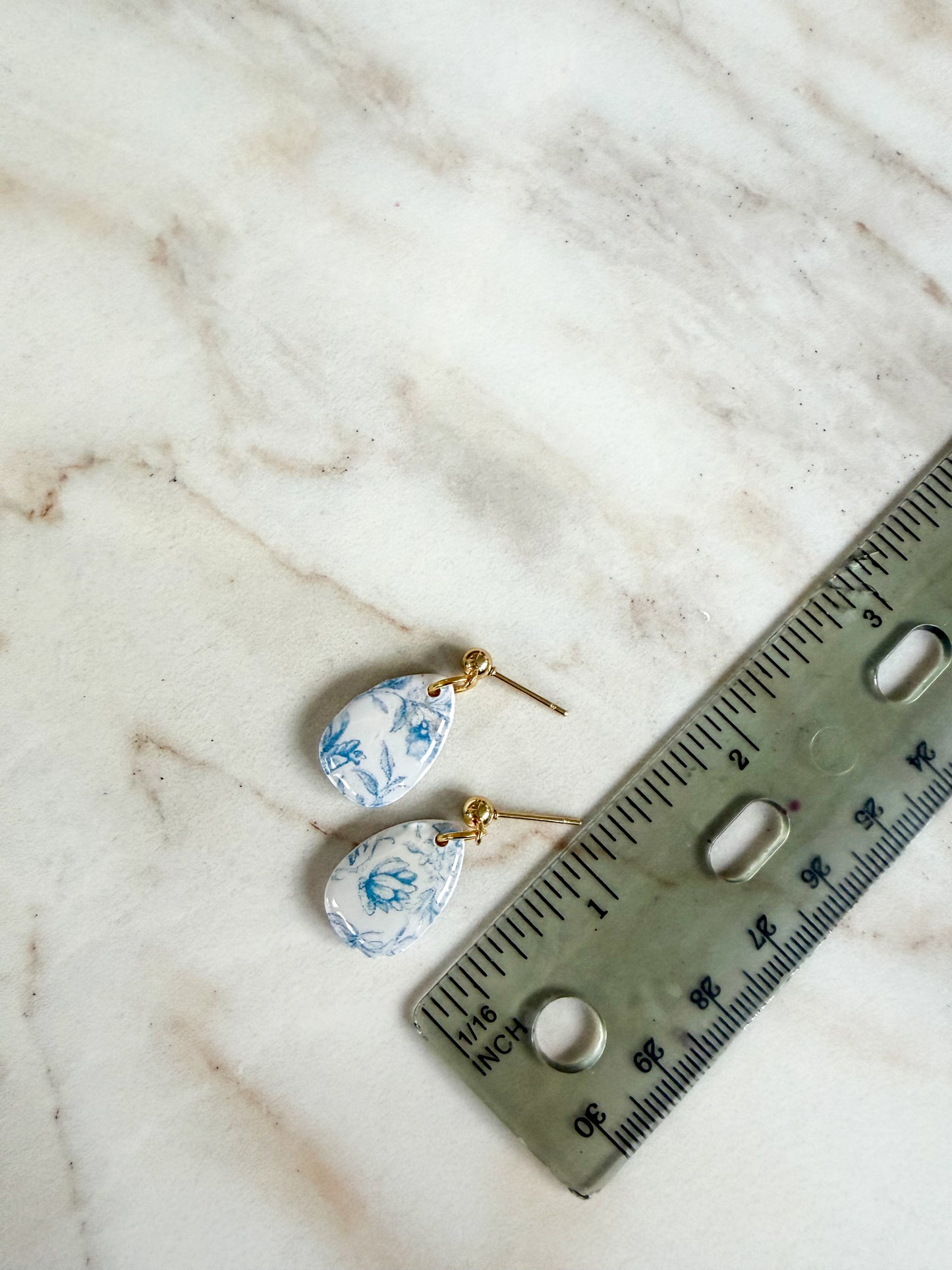 Pair of earrings with blue floral design on a marble surface with a ruler for scale. About one inch in length 