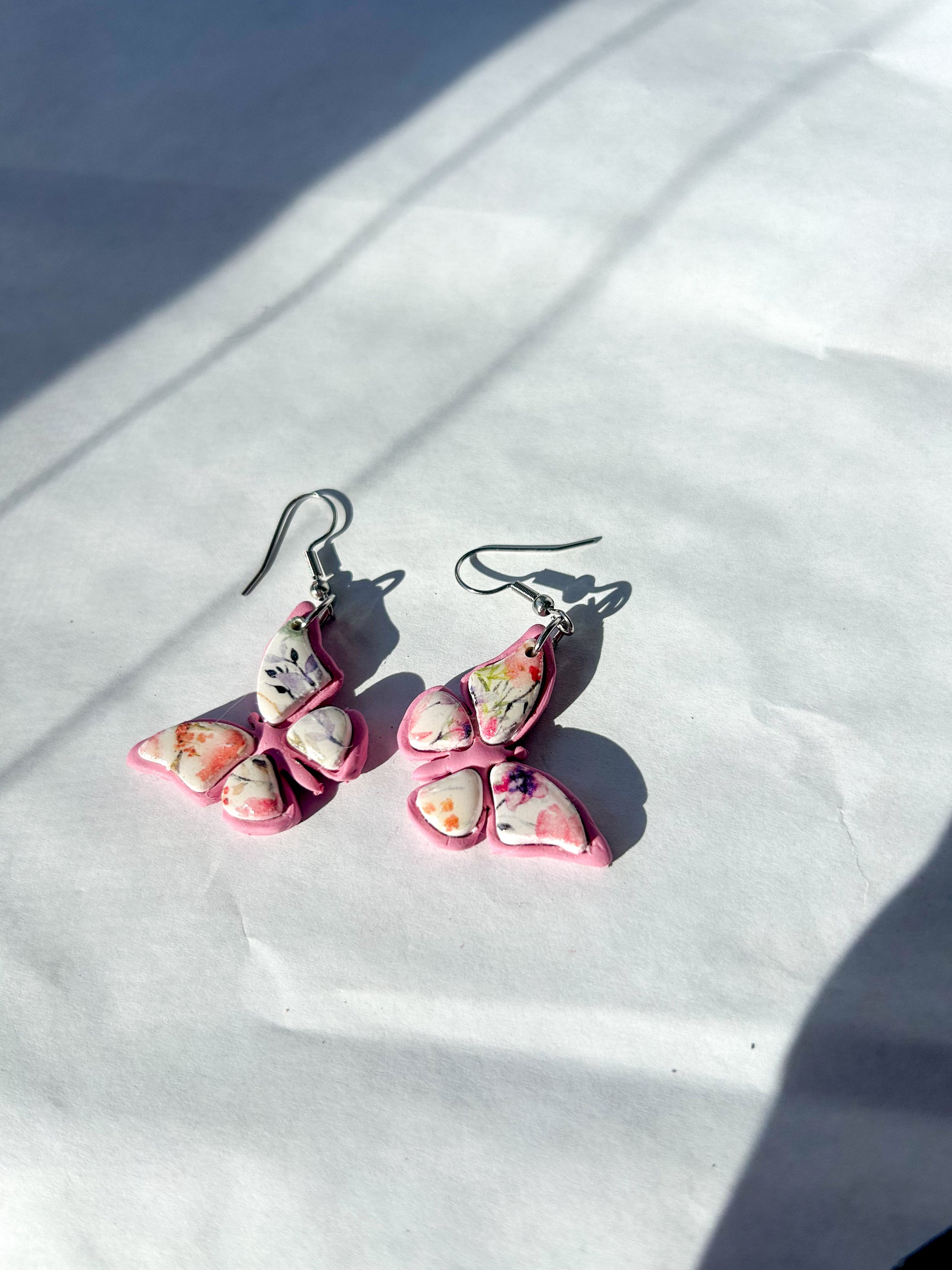 Butterfly-shaped earrings on a white surface with sunlight casting shadows.