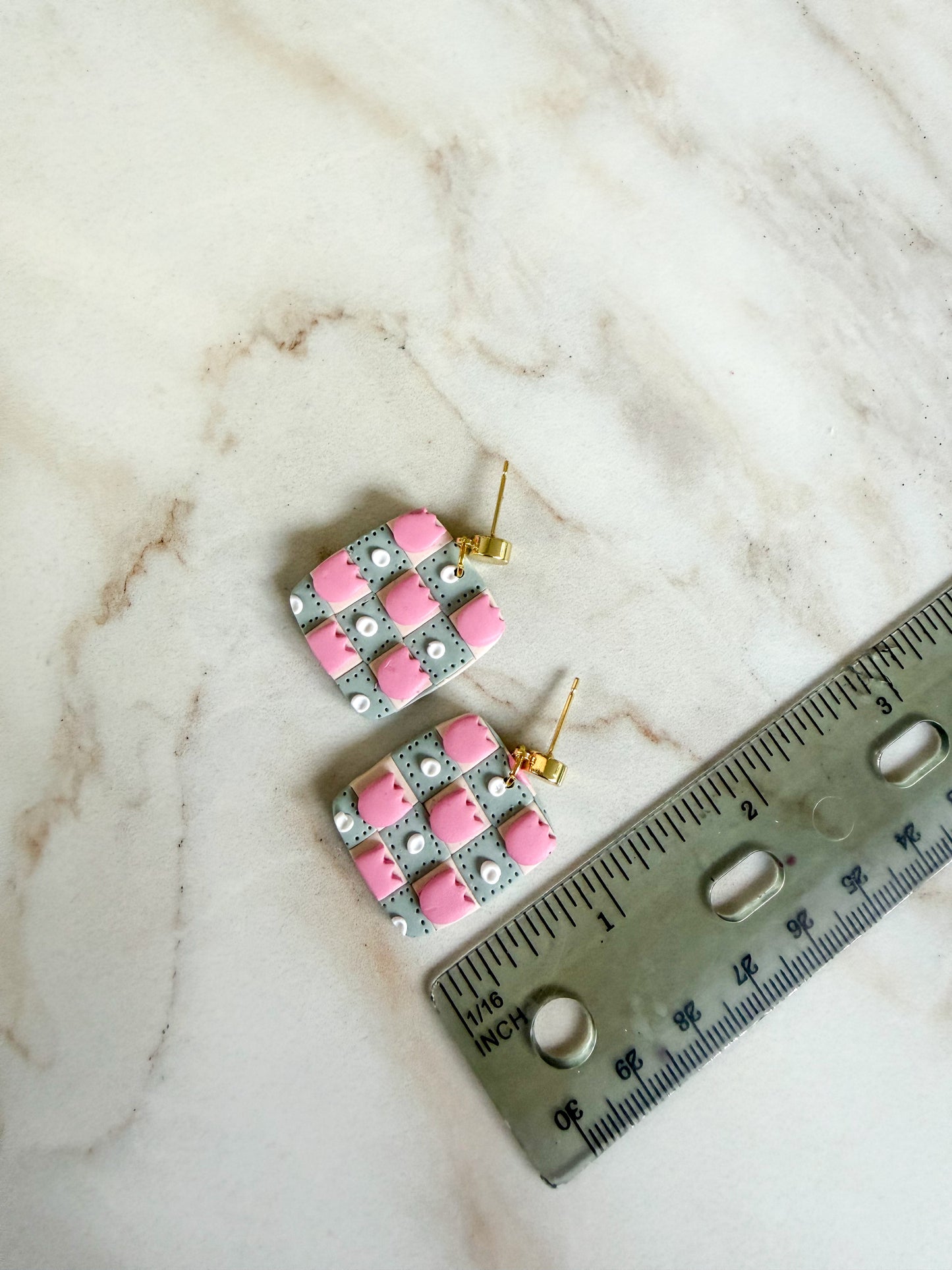 Pair of pink checkered earrings on a marble surface with a ruler for scale. A little over one inch long. 