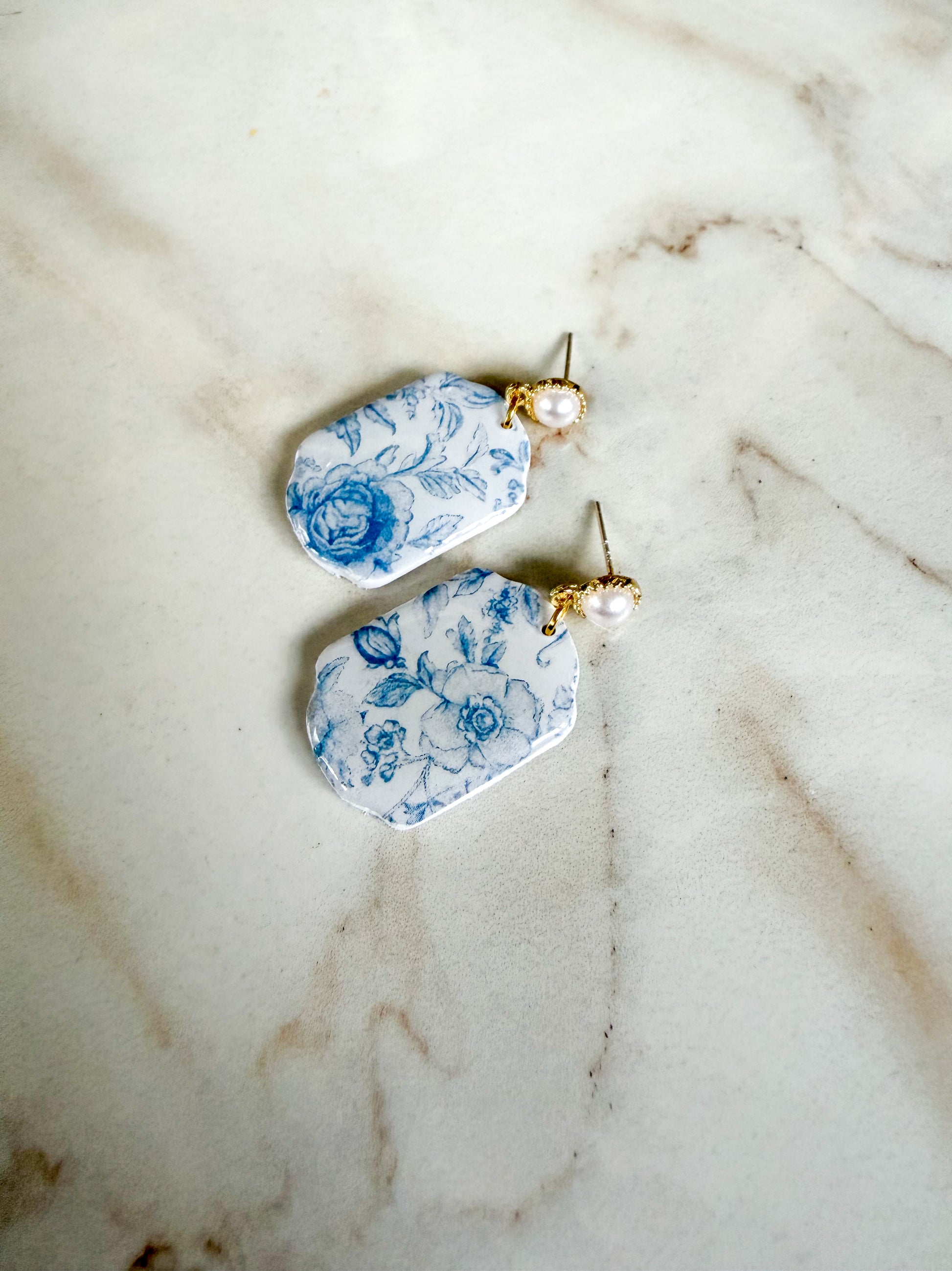 Pair of earrings with blue floral design on a marble surface