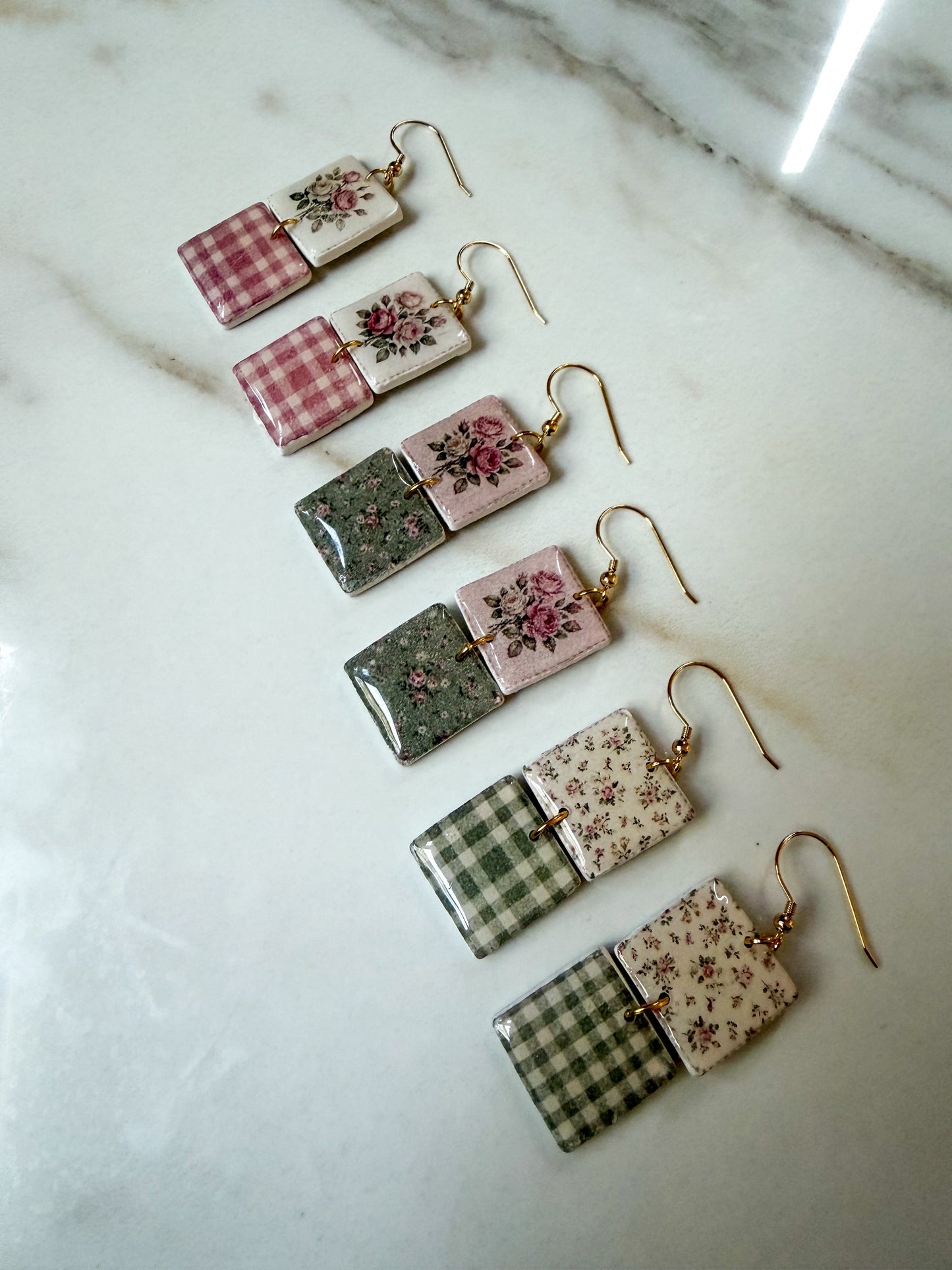 Three pairs of rectangular drop earrings arranged diagonally on a white marble surface. Each pair has one patterned top section and one bottom section, with gold-tone fishhook ear wires.