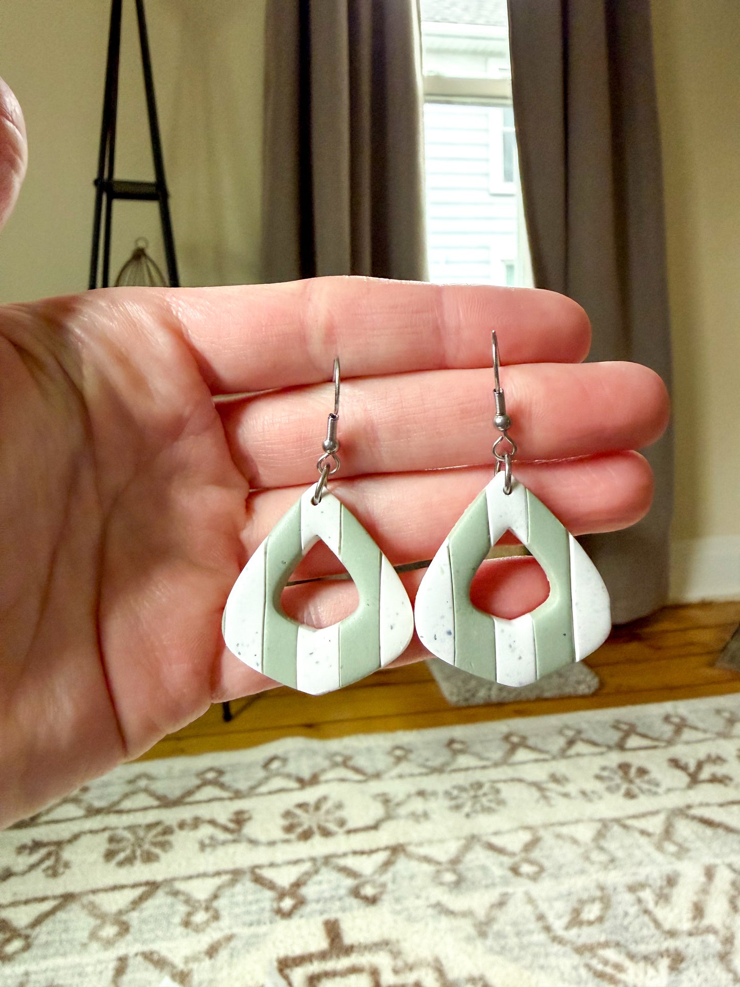 Hand holding a pair of green and white earrings with a neutral background