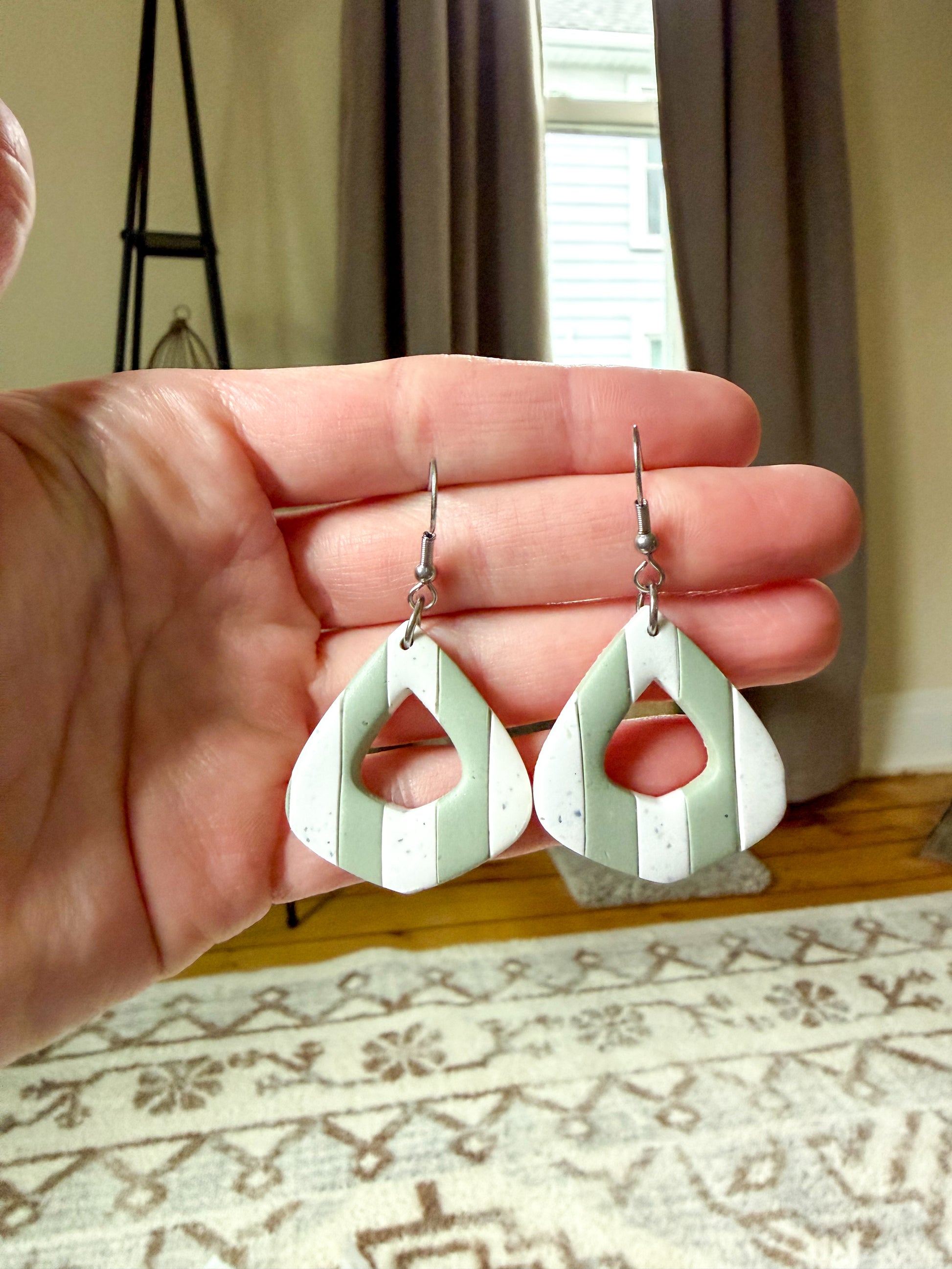 Hand holding a pair of green and white earrings with a neutral background