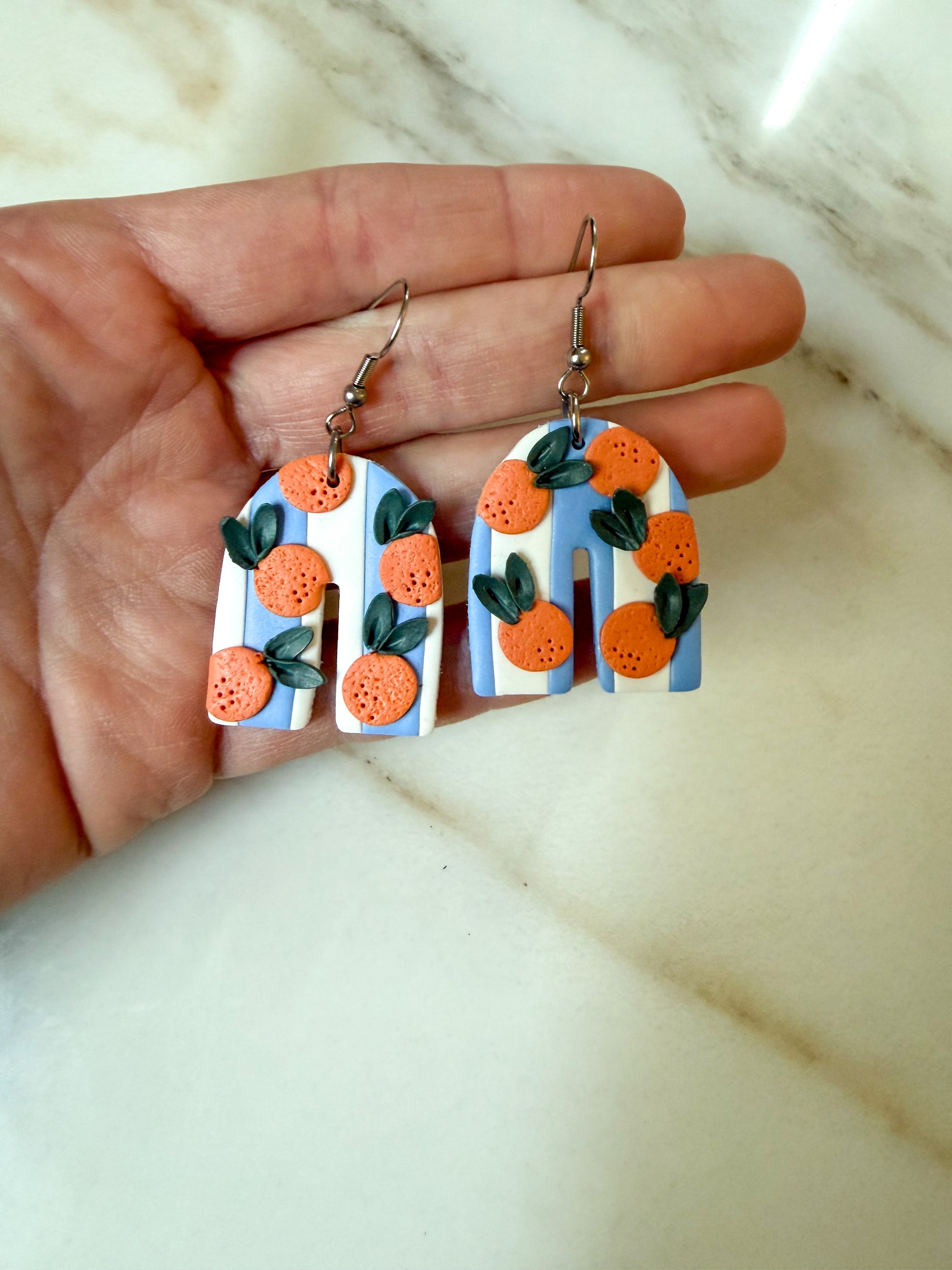A pair of white and blue striped arches with oranges patterned on them. Hypoallergenic stainless steel hooks.